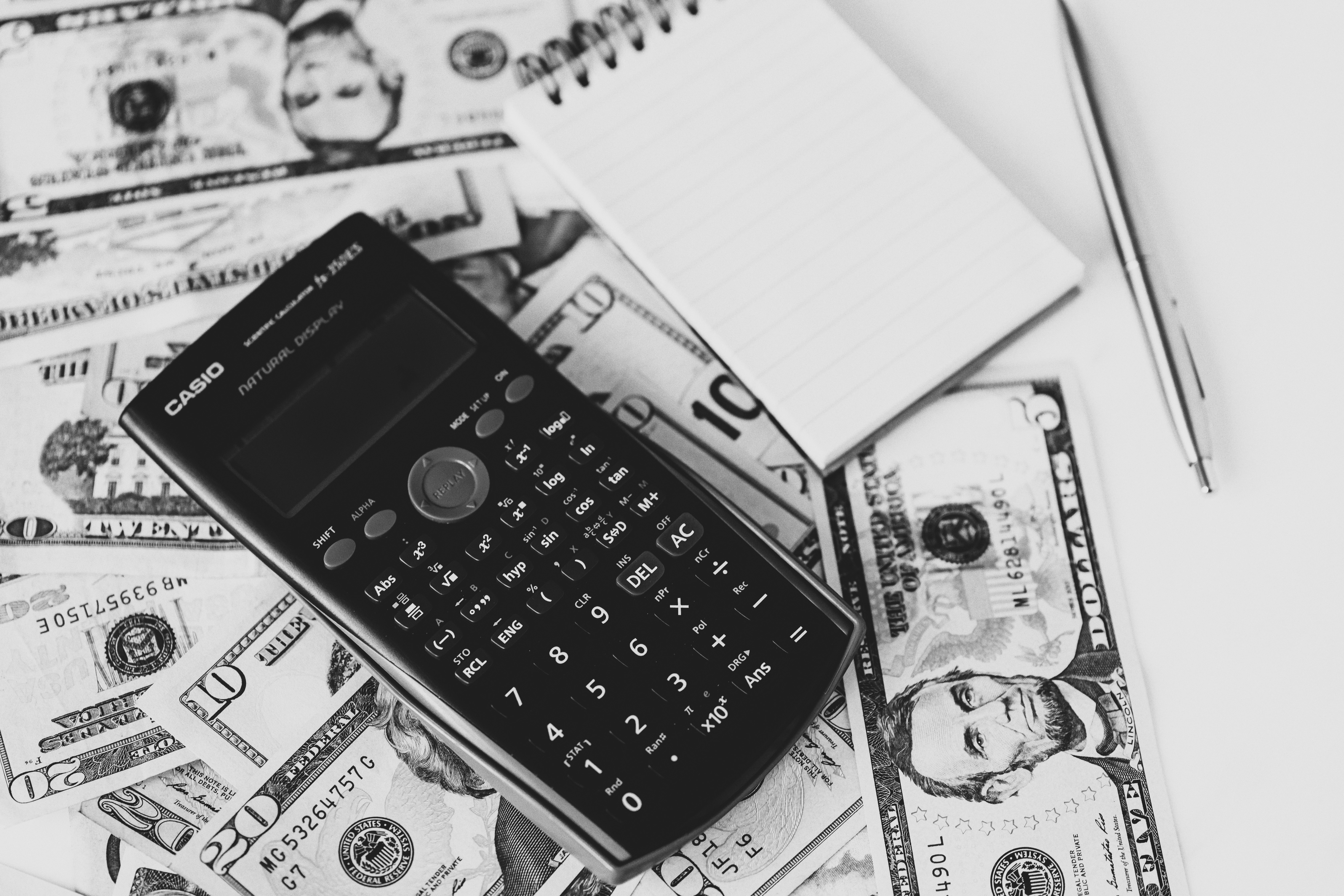 black and white image representing a calculator a notebook and a pen resting on a table with money