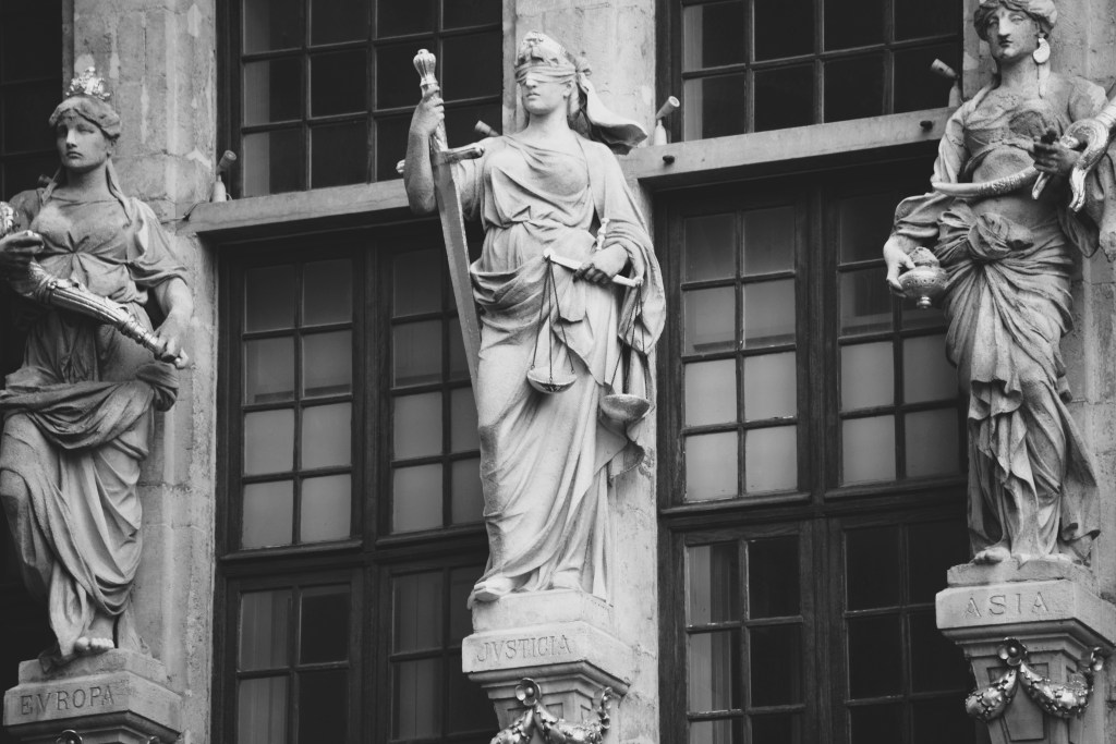 a black-and-white image depicting the goddess of justice dressed in ancient Greek attire and holding a set of scales